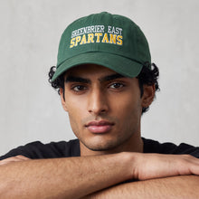 Moco Shirts Greenbrier East Spartans green cotton twill baseball cap worn by a man with arms crossed