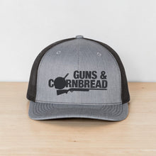 Moco Shirts grey and charcoal mesh back trucker hat with Guns and Cornbread graphic on a tree stump in nature